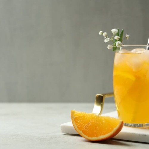 櫛形に切ったオレンジとオレンジのフルーツ酢ドリンクが入ったグラスが置いてある