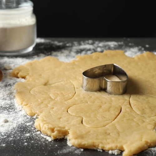 打ち粉をした台の上で米油を使ったクッキー生地をハートの型で型抜きしている。