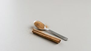 淡いグレーの背景に置いた、すりきり1杯のシナモンパウダーをのせた小さじ