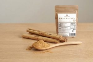 かわしま屋の有機セイロンシナモンパウダー30gの袋と、木のスプーンにのせたパウダー・シナモンスティック